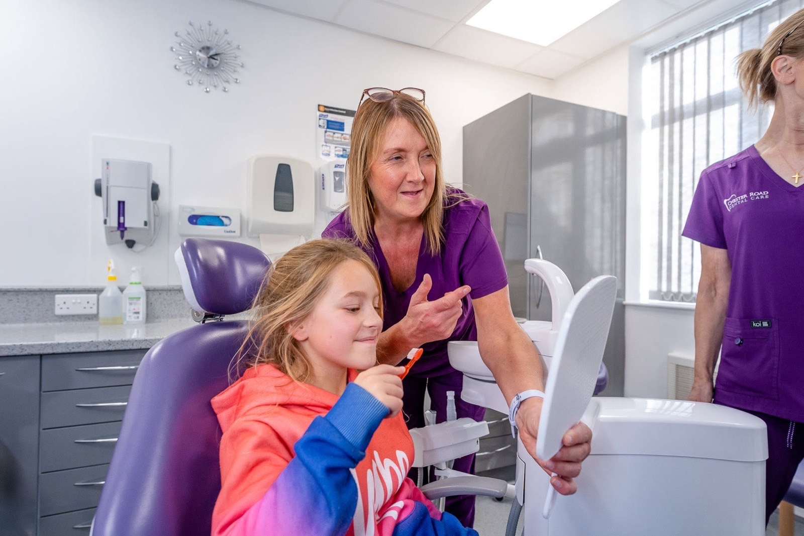 A dental nurse coaching a child on tooth brushing with a hand mirror