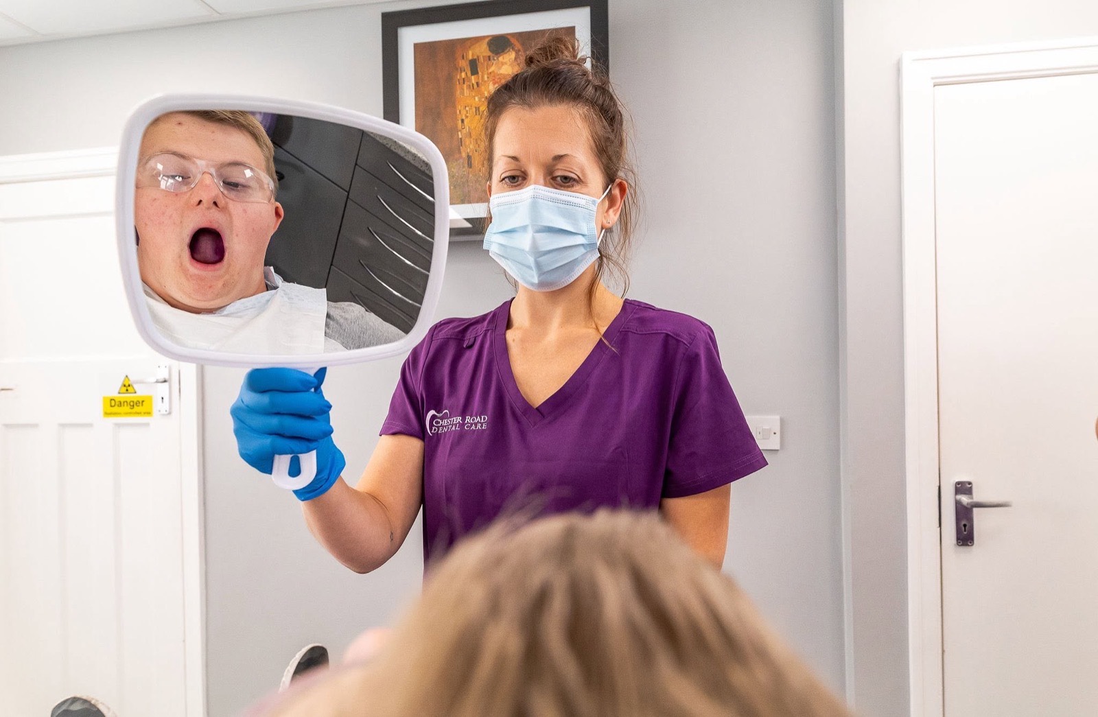 A dental nurse holding a mirror showing a patient's smile during a hygiene visit