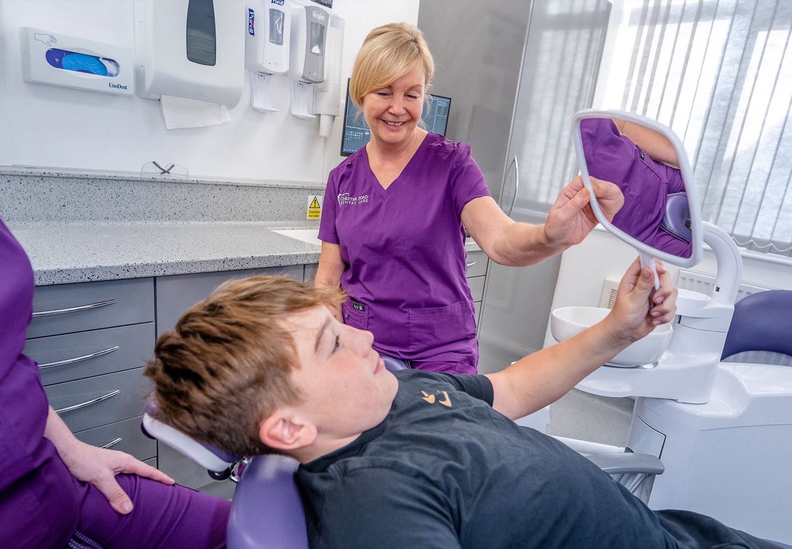 A young patient checking his smile in a hand mirror after treatment